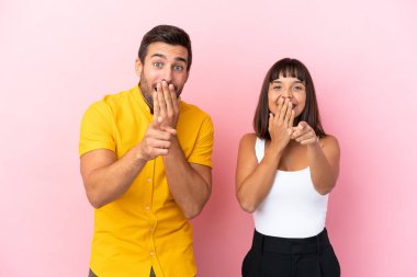 Pembe arka planda izole edilmiş genç bir çift birini işaret ediyor ve gülüyor.
