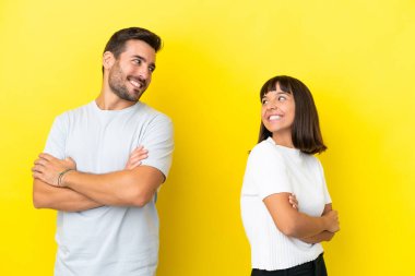 Sarı arka planda izole edilmiş genç bir çift, tebessümle omzunun üstünden bakıyor.