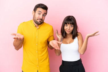 Pembe arka planda yalnız yaşayan genç çift ellerini ve omuzlarını kaldırırken şüphe duyuyorlar.