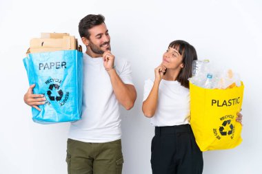 Geri dönüşüm için plastik ve kağıt dolu bir çanta taşıyan genç çift beyaz arka planda izole edilmiş olarak birbirlerine bakıyorlar.