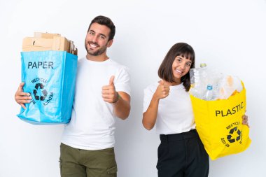 Beyaz arka planda izole edilmiş plastik ve kâğıt dolu bir çanta taşıyan genç çift, iyi bir şey olduğu için olumlu bir hareket yapıyor.