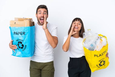 Beyaz arka planda izole edilmiş plastik ve kağıt dolu bir çanta taşıyan genç çift bağırıyor ve bir şey duyuruyor.