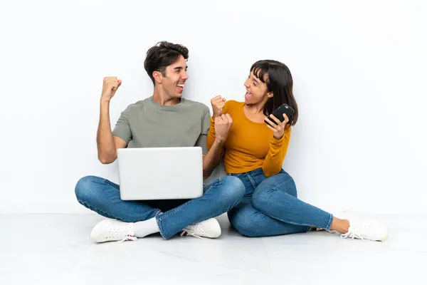 一对年轻的情侣带着笔记本电脑和手机坐在地板上庆祝胜利 — 图库照片