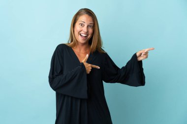 Mavi arka planda izole edilmiş orta yaşlı Brezilyalı kadın şaşırmış ve işaret ediyor.