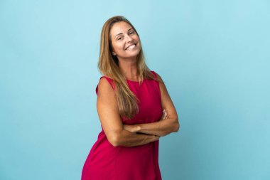 Orta yaşlı Brezilyalı bir kadın mavi arka planda izole edilmiş, kolları bağlı ve ileriye bakıyor.