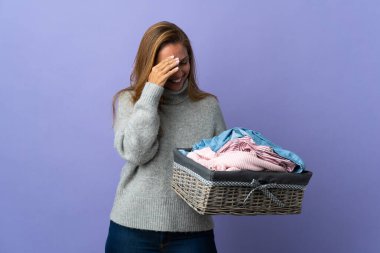 Mor arka planda izole edilmiş çamaşır sepetini tutan orta yaşlı kadın gülüyor.