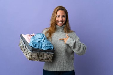 Orta yaşlı bir kadın elinde mor bir arka planda, yüzünde sürpriz bir ifade olan bir çamaşır sepeti tutuyor.
