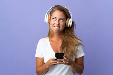 Mor arka planda izole edilmiş orta yaşlı Brezilyalı bir kadın cep telefonuyla müzik dinliyor ve düşünüyor.