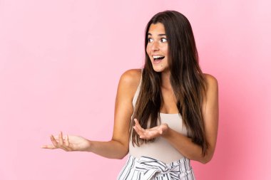 Genç Brezilyalı bir kadın pembe arka planda izole edilmiş. Sürpriz bir ifadeyle yan tarafa bakıyor.