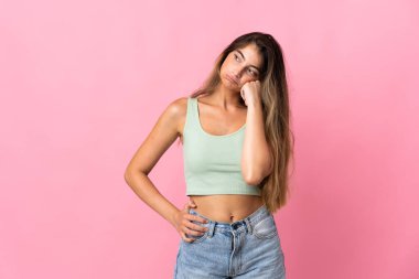 Pembe arka planda soyutlanmış, yorgun ve sıkılmış bir ifadeyle genç beyaz kadın.