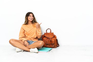 Genç bir bayan öğrenci dizüstü bilgisayarla yerde oturuyor beyaz arka planda izole edilmiş bir şekilde bir ürünü sunmak için kenarı gösteriyor.