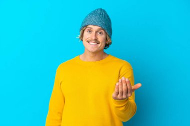 Yakışıklı sarışın adam, mavi arka planda soyutlanmış, davet ediliyor. Gelmene sevindim.