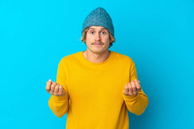 Yakışıklı sarışın adam mavi arka planda izole edilmiş para hareketi yapıyor ama mahvolmuş.