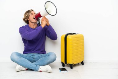 Bavullu genç sarışın adam yerde oturmuş megafonla bağırıyor.