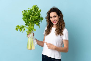 Mavi arka planda izole edilmiş bir kereviz tutan genç bir kadın.