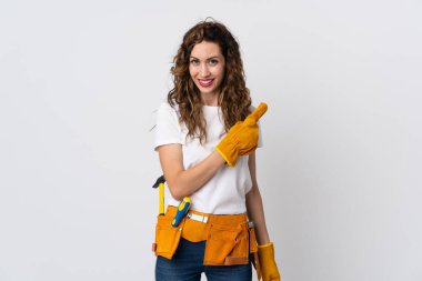 Beyaz arka planda izole edilmiş genç elektrikçi bir ürünü sunmak için kenarı işaret ediyor.