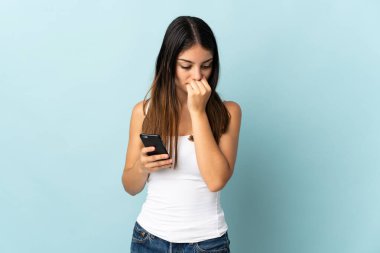 Mavi arka planda izole edilmiş cep telefonu kullanan beyaz bir kadın şüpheleri var.