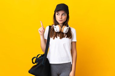 Spor çantalı genç bayan sarı arka planda izole edilmiş bir şekilde parmağını kaldıran bir fikir düşünüyor.