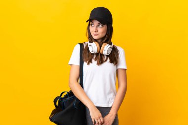 Sarı arka planda izole edilmiş spor çantalı genç bayan şüpheli hareketler yapıyor.