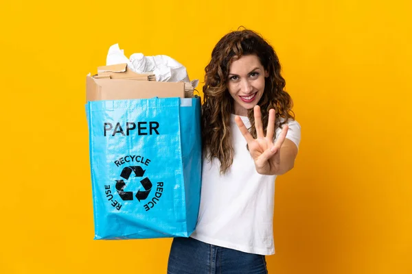 黄色の背景に隔離されたリサイクル紙の袋を持っている若い女性幸せと指で4を数える — ストック写真