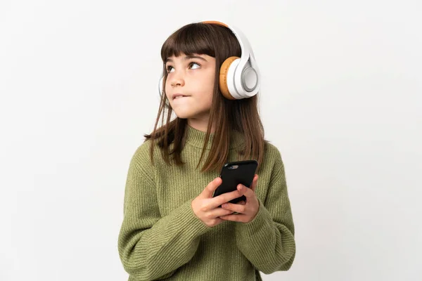 白い背景で隔離された携帯電話で音楽を聴いている女の子モバイルと思考で音楽を聴いている — ストック写真