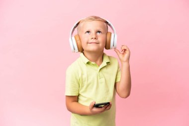 Küçük Rus çocuk pembe arka planda izole edilmiş müzik dinliyor ve şarkı söylüyor.