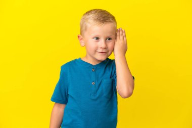 Küçük Rus çocuk sarı arka planda izole edilmiş. Kulağına elini sürerek bir şeyler dinliyor.