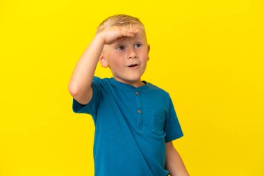 Sarı arka planda izole edilmiş küçük Rus çocuk yan tarafa bakarken sürpriz jest yapıyor.