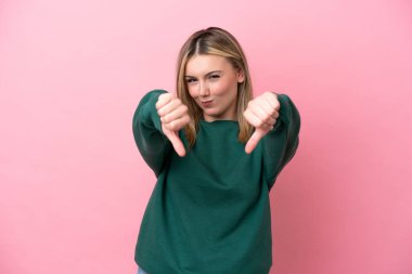 Pembe arka planda izole edilmiş beyaz bir kadın baş parmağını iki eliyle aşağı gösteriyor.