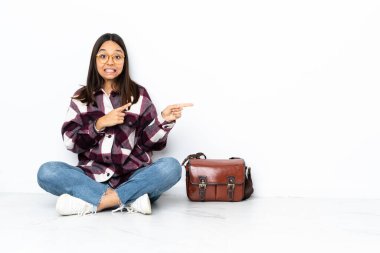 Genç bir kız öğrenci yerde oturuyor, korkmuş ve onu işaret ediyor.