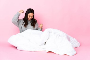 Genç melez kadın pijama giymiş yerde oturmuş zaferi kutluyor.