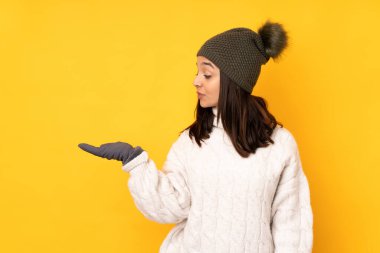 Sarı arka plan üzerinde kışlık şapkası olan genç bir kadın boşluğu kuşkuyla dolduruyor.
