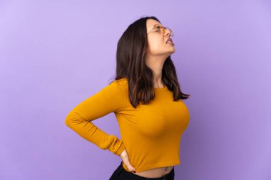 Mor arka planda izole edilmiş genç melez kadın gayret gösterdiği için sırt ağrısından muzdarip.