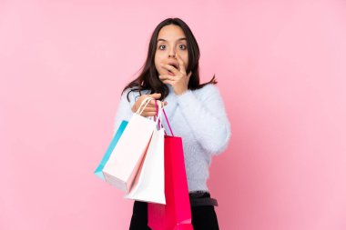 Soyutlanmış pembe arka planda alışveriş çantası taşıyan genç bir kadın sağa bakarken şaşırmış ve şok olmuştu.