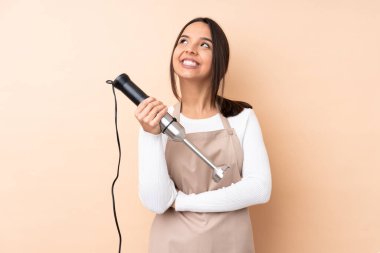 El blenderi kullanan genç esmer kız izole edilmiş arka planda gülümserken yukarı bakıyor.