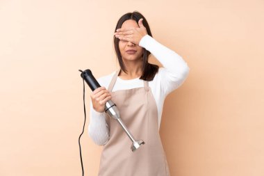 Genç esmer kız, el blendırını izole edilmiş arka plan üzerinde kullanıyor. Gözlerini elleriyle kapatıyor. Bir şey görmek istemiyorum.