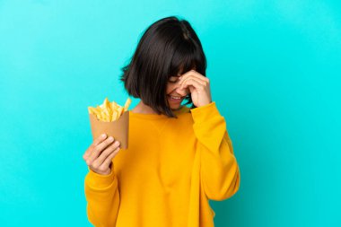 Genç esmer kadın izole edilmiş mavi arka planda kızarmış patates kızartması tutuyor.