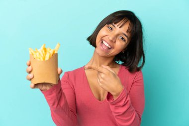 Genç esmer kadın izole edilmiş mavi arka planda patates kızartması tutuyor.