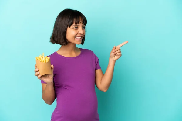 Kobieta Ciąży Trzyma Smażone Żetony Pojedynczym Tle Wskazując Palcem Bok — Zdjęcie stockowe
