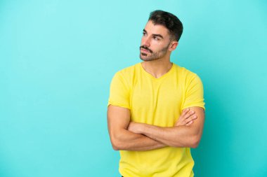 Mavi arka planda izole edilmiş genç beyaz adam yan tarafa bakıyor.