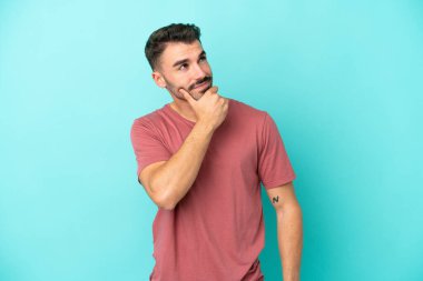 Kafkasyalı genç adam mavi arka planda izole edilmiş bir şekilde yukarı bakarken bir fikir düşünüyor.