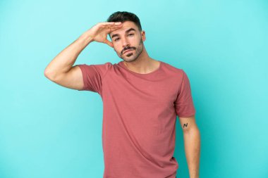 Kafkasyalı genç bir adam mavi arka planda izole edilmiş. Bir şeye bakmak için uzaklara bakıyor.