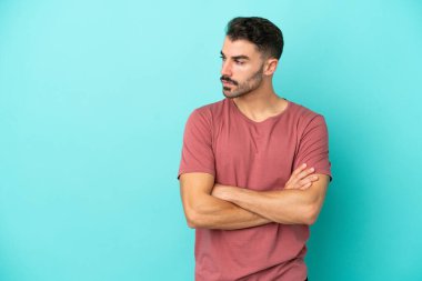 Mavi arka planda izole genç beyaz adam kollarını çapraz tutuyor.