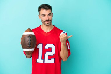 Rugby oynayan beyaz bir genç, mavi arka planda izole edilmiş bir şekilde bir ürünü sunmak için yan tarafa bakıyor.