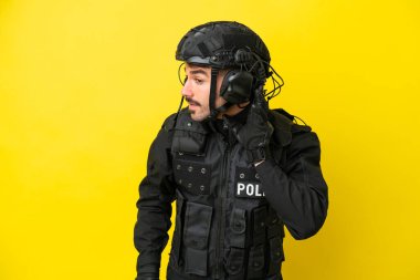 Özel Tim 'in beyaz adamı sarı arka planda izole edilmiş bir şekilde kulağına elini sürerek bir şeyler dinliyor.