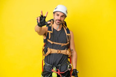 Sarı arka planda izole edilmiş beyaz dağcı mutlu ve parmaklarıyla üçe kadar sayıyor.