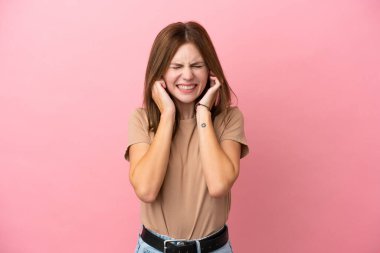 Pembe arka planda izole edilmiş genç bir İngiliz kadın hayal kırıklığına uğramış ve kulaklarını kapatmış.