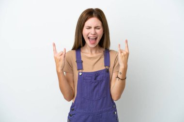 Beyaz arka planda izole edilmiş genç bir İngiliz kadın boynuz hareketi yapıyor.