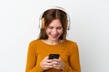 Genç İngiliz kadın beyaz arka planda izole edilmiş müzik dinliyor ve cep telefonu arıyor.