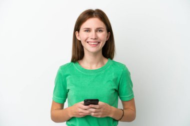 Beyaz arka planda izole edilmiş genç bir İngiliz kadın kameraya bakıyor ve cep telefonunu kullanırken gülümsüyor.